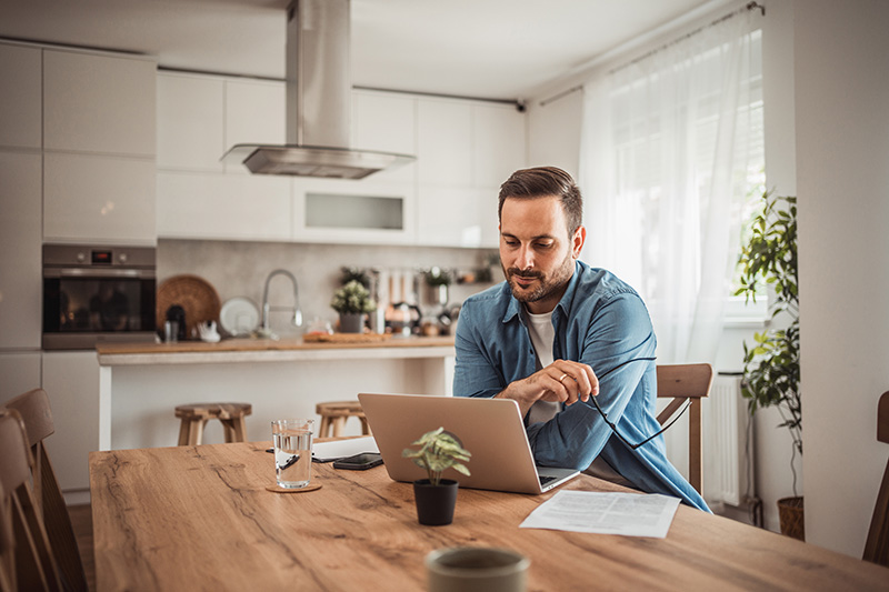 Man at his kitchen table with a laptop, considering the benefits of a Roth IRA Conversion.